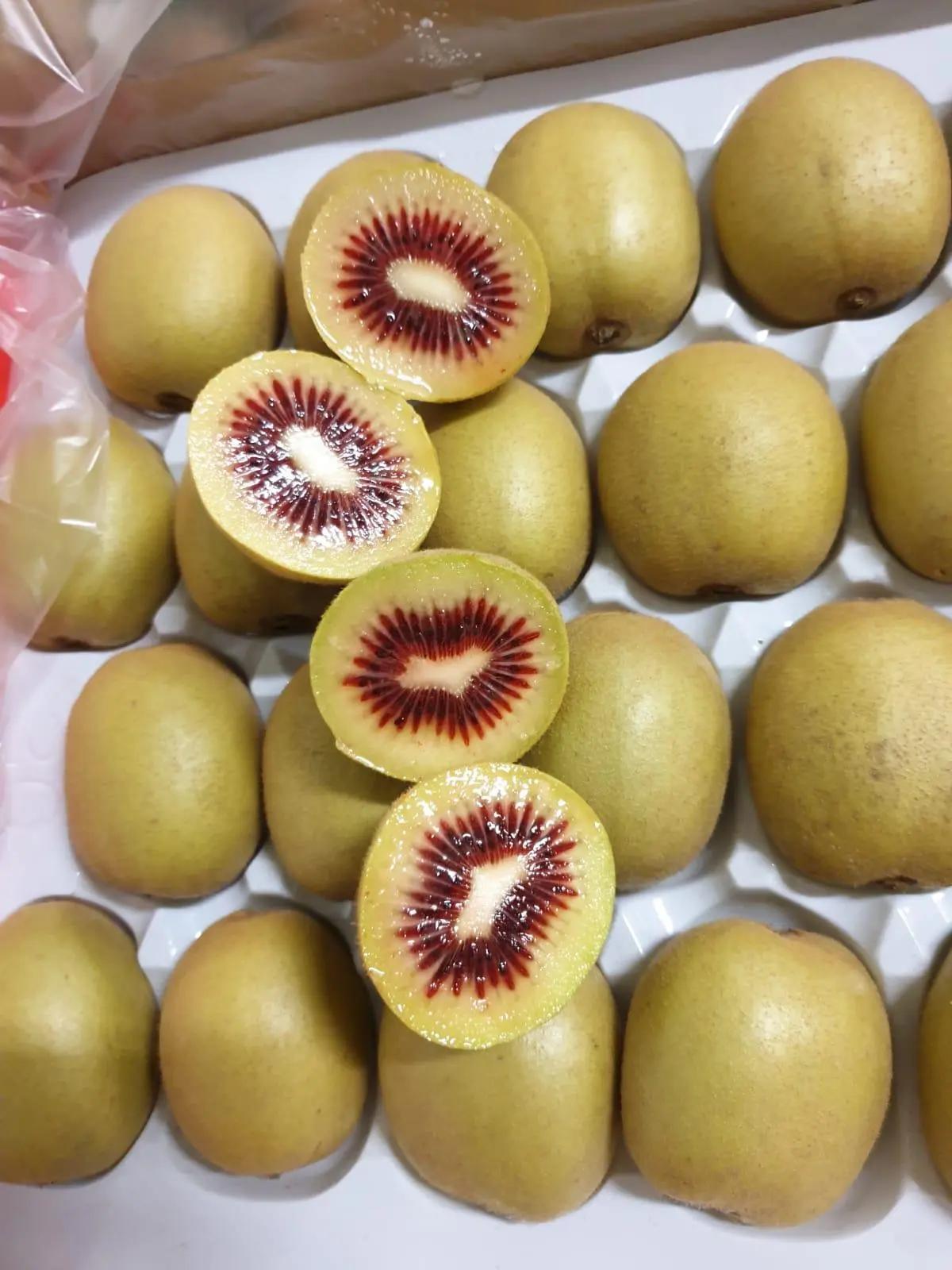 Kiwis rouges entiers et en tranches sur une surface blanche.