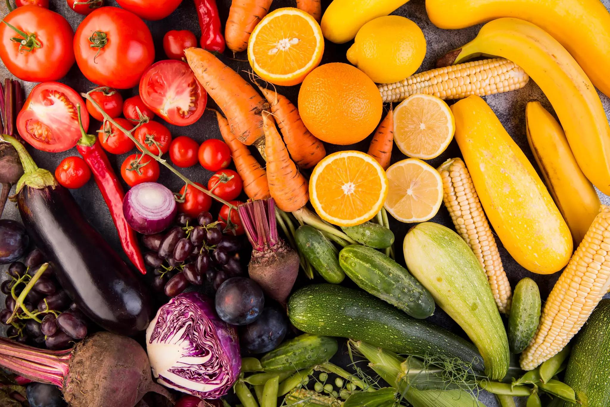 Assortiment de légumes et de fruits frais, dont des tomates, des carottes et des oranges.