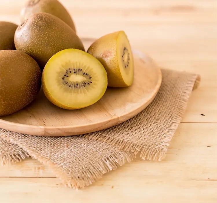 Des kiwis jaunes sunlife entiers et en tranches sur un plateau en bois avec une toile de jute.