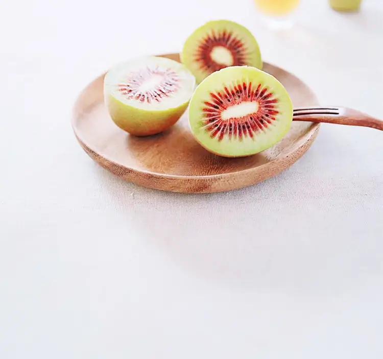 Kiwis rouges rossy sur une assiette en bois prêt a être dégusté à l'aide d'une fourchette en bois.